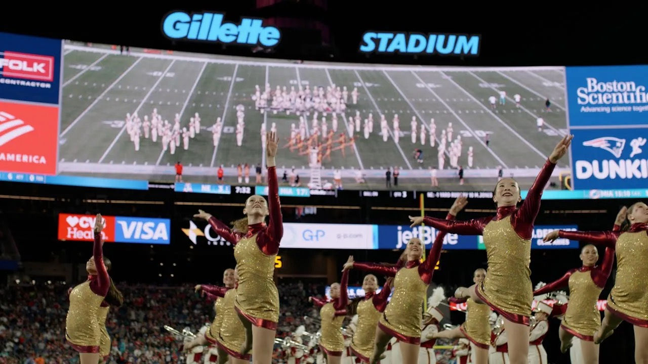 Dancers on the football field with marching band on the jumbotron